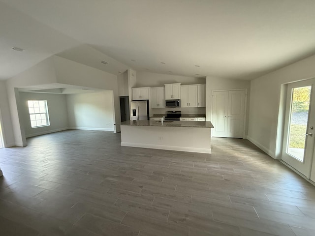 kitchen with lofted ceiling, white cabinetry, a center island with sink, dark stone counters, and stainless steel appliances