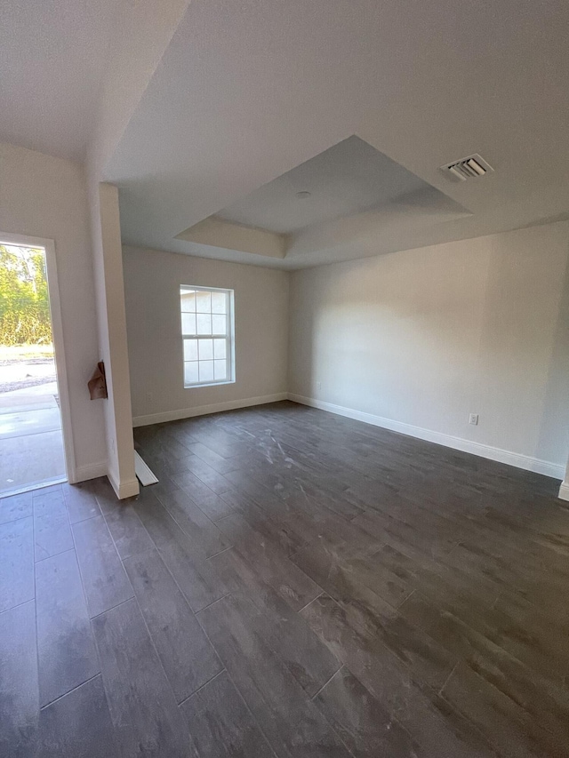 unfurnished room featuring a healthy amount of sunlight, dark hardwood / wood-style floors, and a raised ceiling