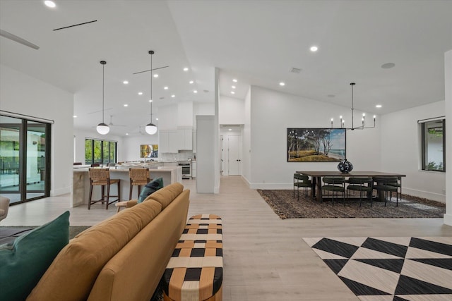 living room with high vaulted ceiling, a notable chandelier, and light wood-type flooring