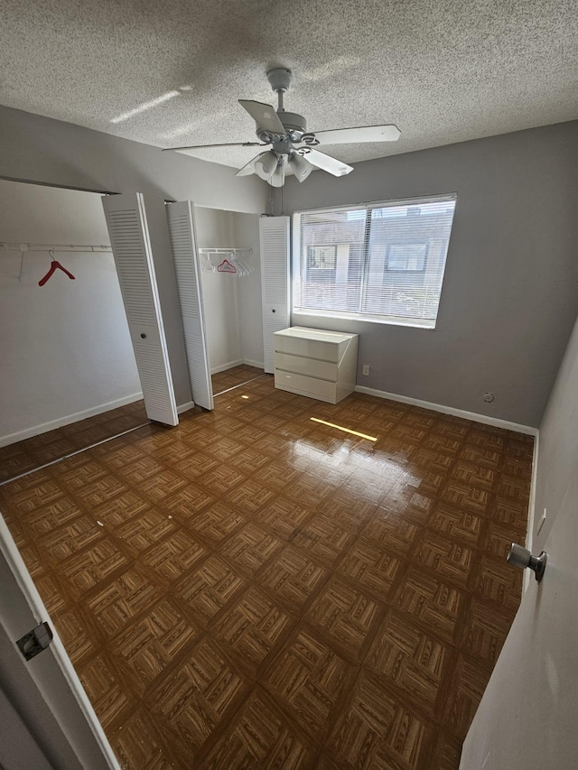 unfurnished bedroom featuring multiple closets, a textured ceiling, dark parquet flooring, and ceiling fan