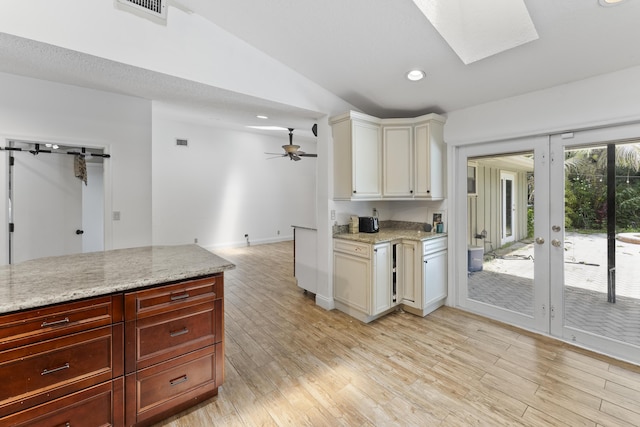 kitchen featuring vaulted ceiling with skylight, ceiling fan, light stone counters, and light hardwood / wood-style flooring