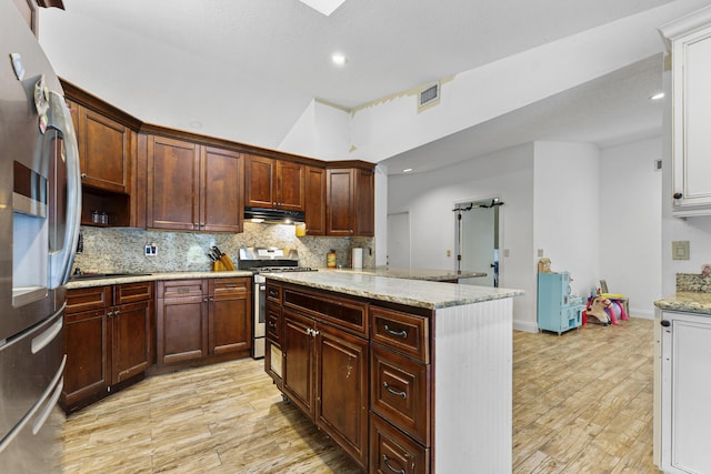 kitchen with light stone countertops, light hardwood / wood-style flooring, a kitchen island, and stainless steel appliances