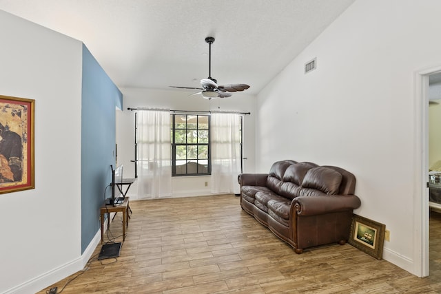 living room with ceiling fan, vaulted ceiling, a textured ceiling, and light hardwood / wood-style flooring