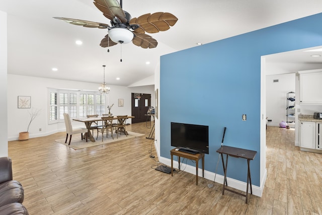 living room featuring ceiling fan with notable chandelier, light hardwood / wood-style floors, and vaulted ceiling