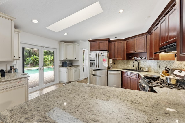 kitchen featuring light stone countertops, french doors, a skylight, stainless steel appliances, and sink