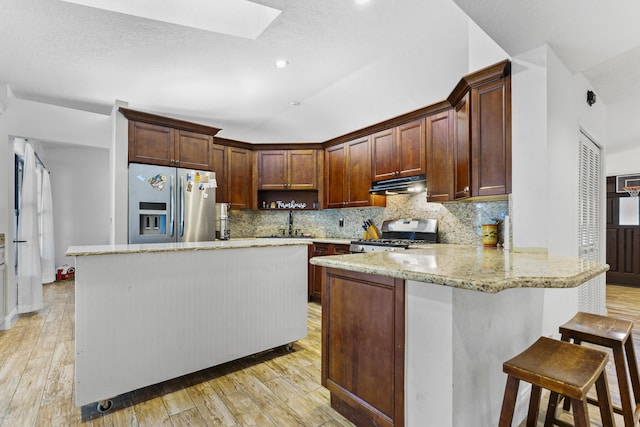 kitchen featuring kitchen peninsula, stainless steel fridge, light hardwood / wood-style flooring, range, and a breakfast bar area