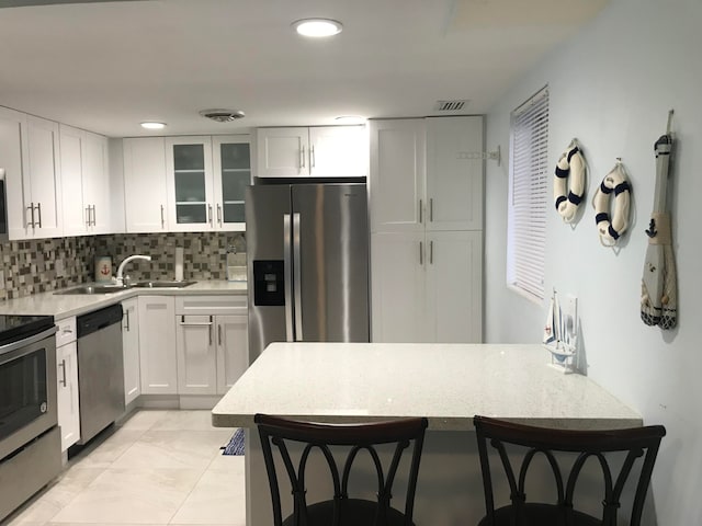 kitchen with appliances with stainless steel finishes, white cabinetry, a breakfast bar area, and sink