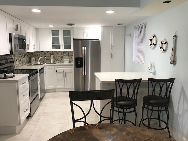 kitchen featuring stainless steel appliances, sink, decorative backsplash, a breakfast bar area, and white cabinets