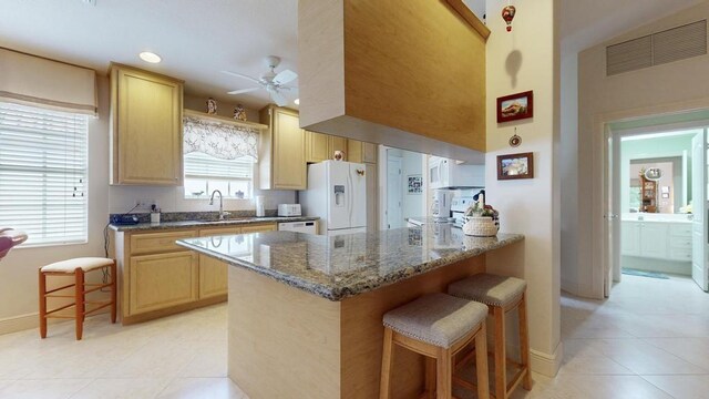 kitchen featuring dark stone countertops, a kitchen breakfast bar, white fridge with ice dispenser, kitchen peninsula, and light brown cabinets