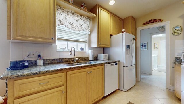 kitchen with sink, white appliances, dark stone counters, and backsplash