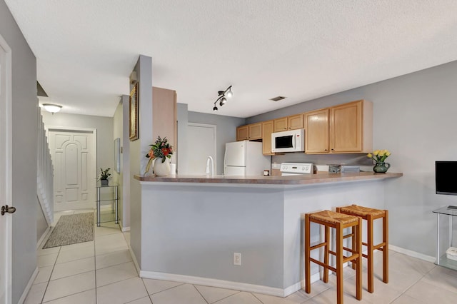 kitchen with kitchen peninsula, white appliances, a textured ceiling, light brown cabinets, and a breakfast bar area