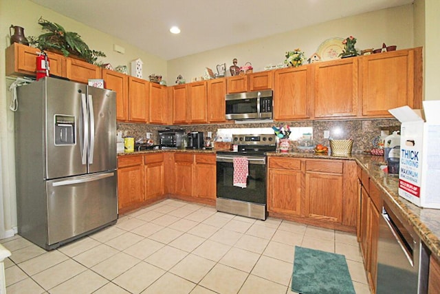 kitchen featuring decorative backsplash, light tile patterned floors, dark stone counters, and appliances with stainless steel finishes