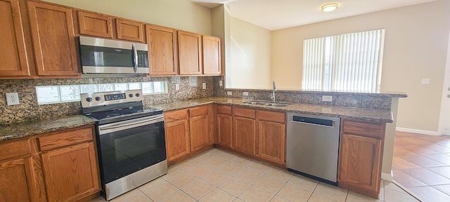 kitchen featuring sink, backsplash, kitchen peninsula, light tile patterned floors, and appliances with stainless steel finishes