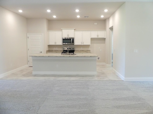 kitchen featuring stainless steel appliances, light stone counters, light carpet, a center island with sink, and white cabinets