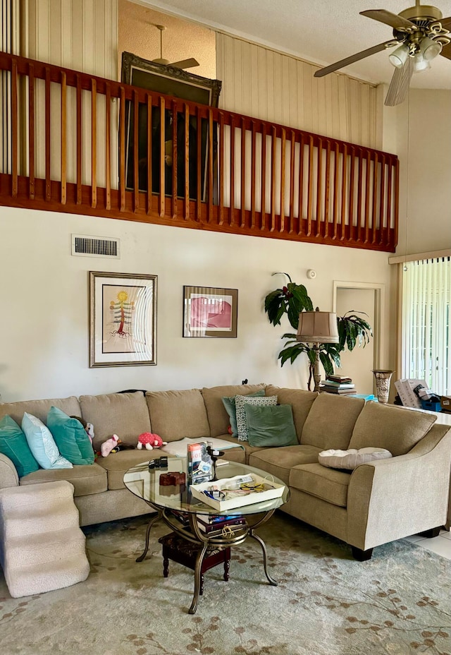 living room featuring ceiling fan, a high ceiling, and visible vents