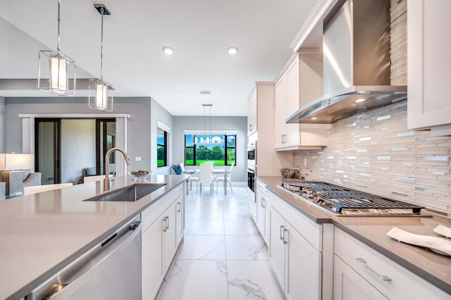 kitchen featuring tasteful backsplash, decorative light fixtures, sink, appliances with stainless steel finishes, and wall chimney range hood