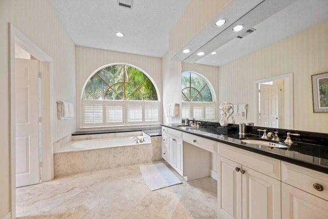 bathroom with tiled tub, a textured ceiling, and vanity