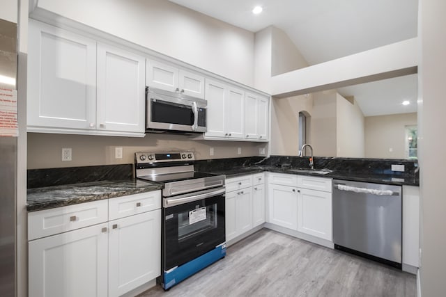 kitchen with stainless steel appliances, white cabinets, sink, light hardwood / wood-style flooring, and dark stone countertops