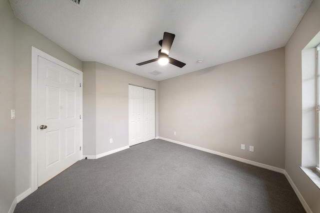 unfurnished bedroom with ceiling fan, dark colored carpet, and a closet