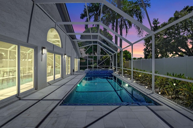 pool at dusk with glass enclosure and a patio area