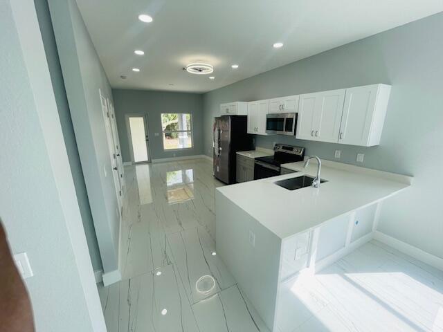 kitchen with stainless steel appliances, white cabinetry, sink, and kitchen peninsula