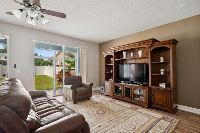 living room with a textured ceiling, ceiling fan, and light wood-type flooring