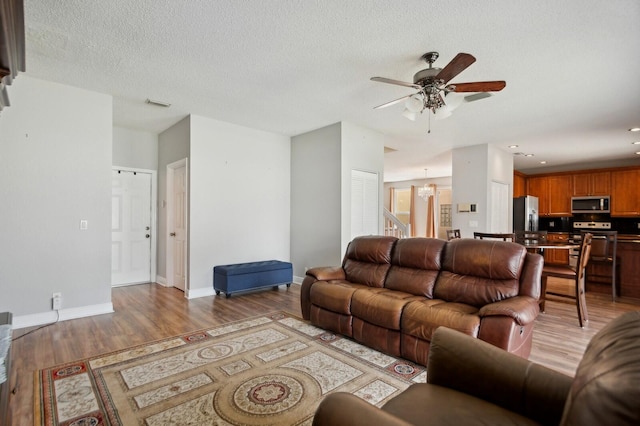 living room with ceiling fan with notable chandelier, light hardwood / wood-style floors, and a textured ceiling