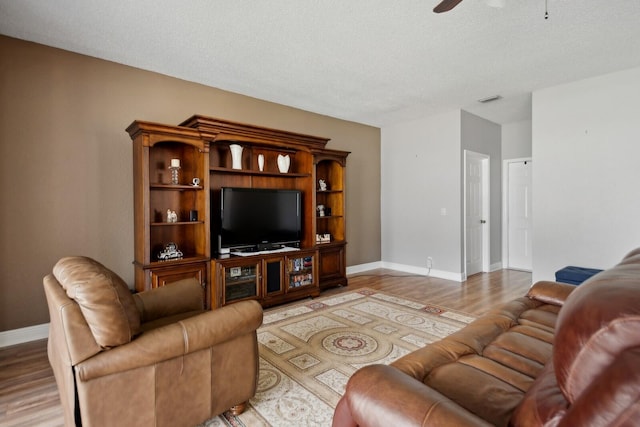 living room with a textured ceiling, ceiling fan, and light hardwood / wood-style floors