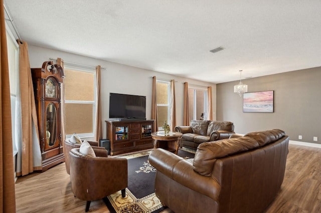 living room with a wealth of natural light, light hardwood / wood-style floors, a notable chandelier, and a textured ceiling