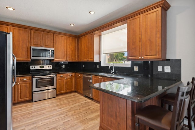 kitchen with light wood-type flooring, stainless steel appliances, sink, kitchen peninsula, and a breakfast bar area