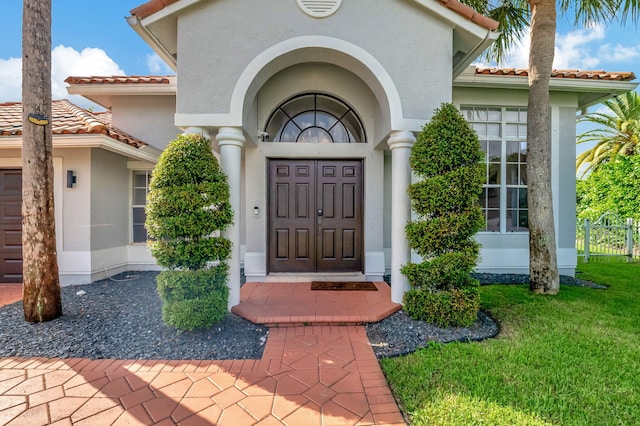 entrance to property featuring a garage, a yard, a tile roof, and stucco siding