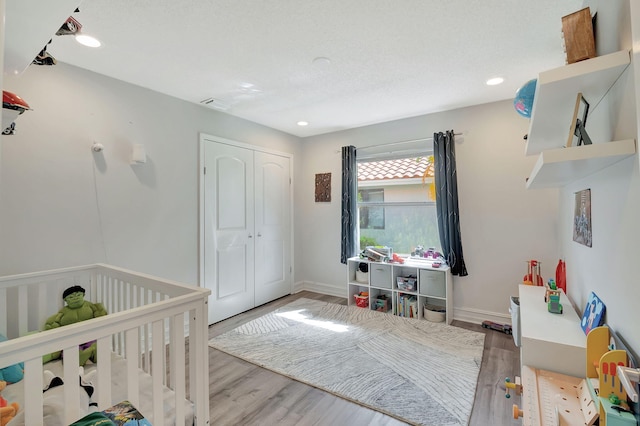 bedroom featuring a textured ceiling, a nursery area, a closet, and light hardwood / wood-style floors