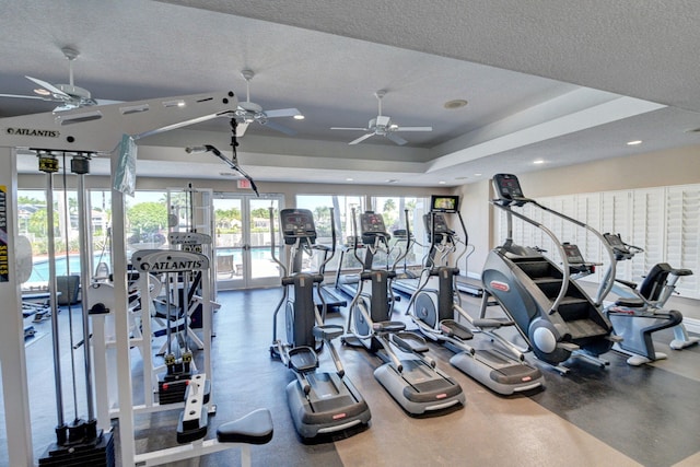 exercise room featuring a tray ceiling, french doors, a textured ceiling, and ceiling fan