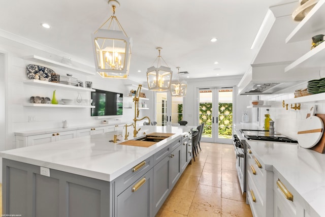 kitchen with pendant lighting, an island with sink, sink, light stone countertops, and french doors