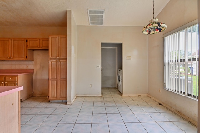 kitchen featuring washer / dryer, a textured ceiling, hanging light fixtures, and light tile patterned floors