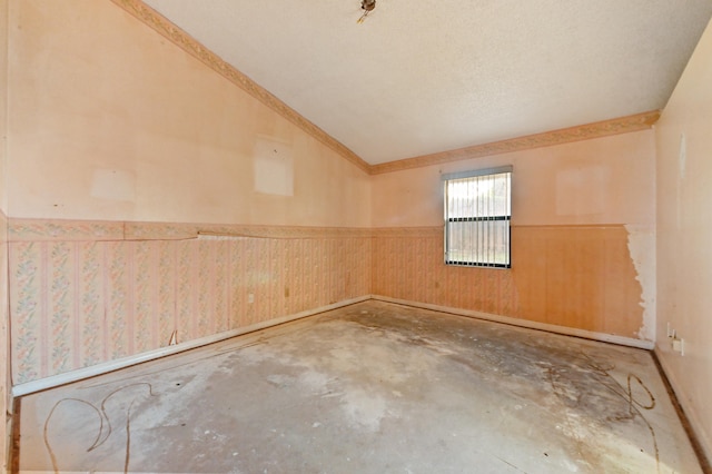 unfurnished room with lofted ceiling, wood walls, concrete flooring, and a textured ceiling