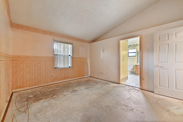 unfurnished room featuring a textured ceiling, wooden walls, and vaulted ceiling