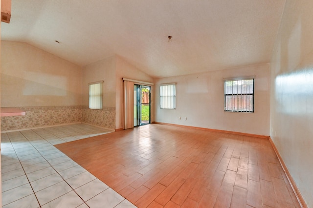 empty room featuring light hardwood / wood-style flooring, a textured ceiling, and vaulted ceiling