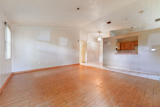 empty room featuring lofted ceiling, a textured ceiling, and light wood-type flooring