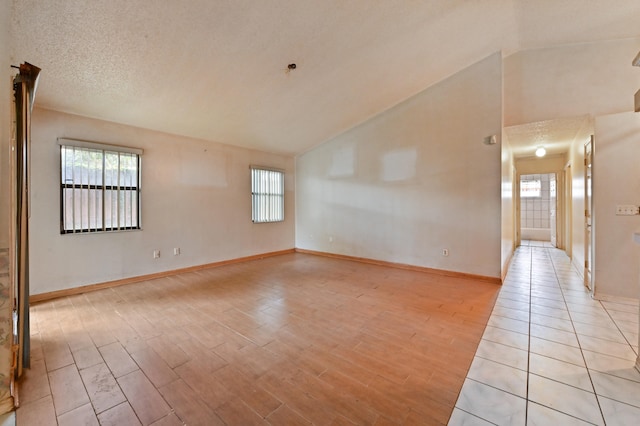 unfurnished room with lofted ceiling, a textured ceiling, and light wood-type flooring