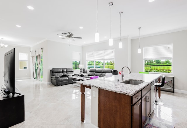 kitchen with a kitchen island with sink, crown molding, sink, light stone countertops, and ceiling fan