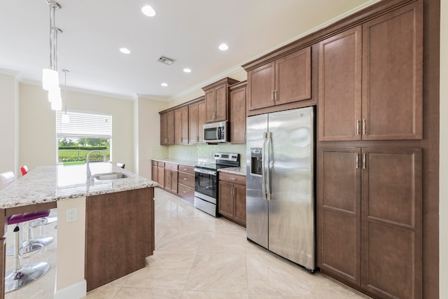 kitchen with light stone countertops, backsplash, a kitchen island with sink, stainless steel appliances, and sink