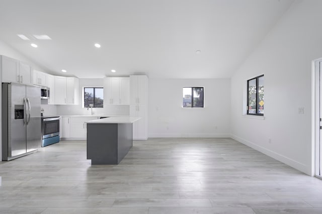 kitchen featuring lofted ceiling, stainless steel appliances, light countertops, white cabinetry, and a sink