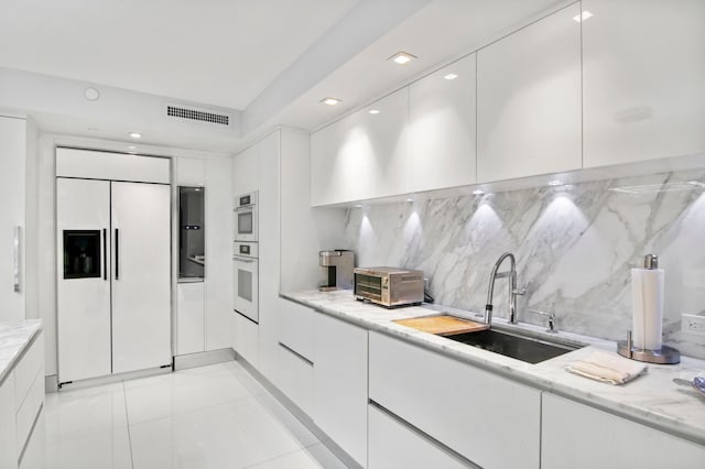 kitchen featuring white cabinets, paneled fridge, sink, and light stone countertops