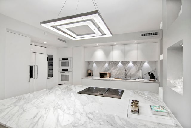 kitchen with light stone counters, white double oven, decorative backsplash, and black electric cooktop