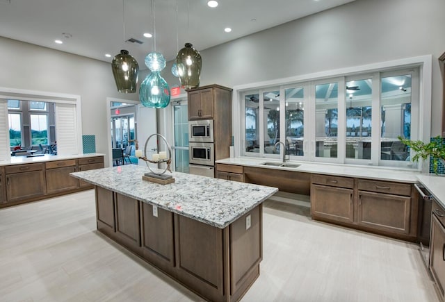 kitchen with stainless steel microwave, oven, light stone countertops, a kitchen island, and sink