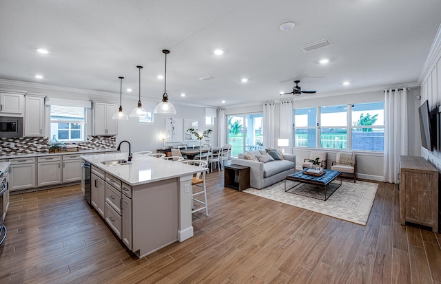 kitchen featuring ceiling fan, a kitchen bar, sink, hanging light fixtures, and an island with sink