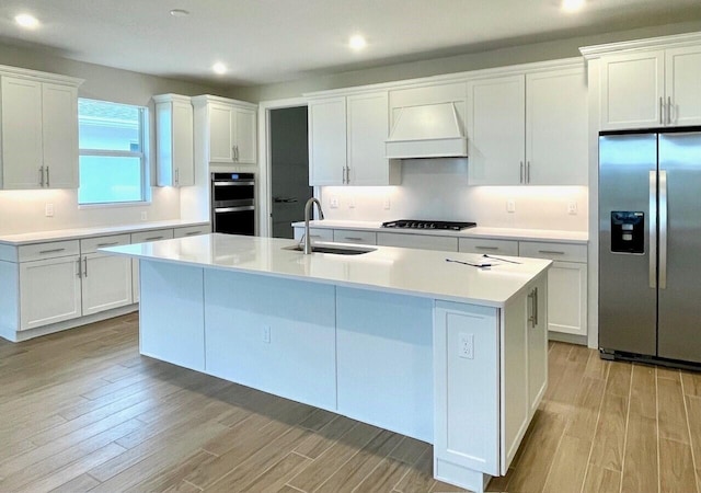 kitchen with a kitchen island with sink, sink, stainless steel appliances, and white cabinetry