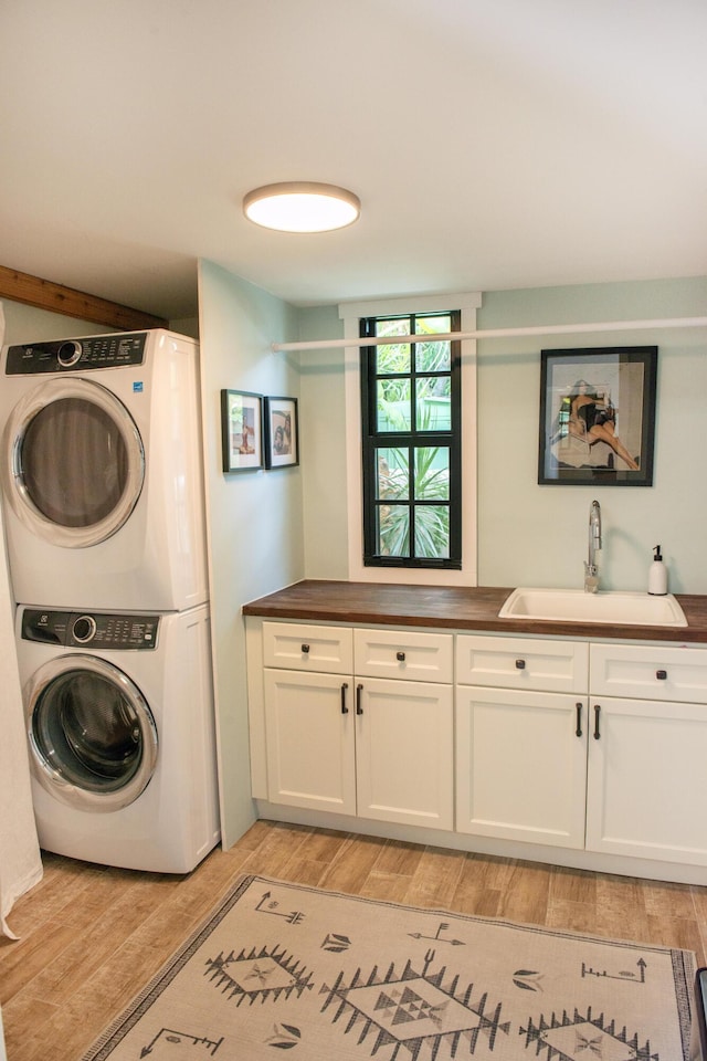 laundry room featuring cabinet space, stacked washer / drying machine, light wood-style floors, and a sink