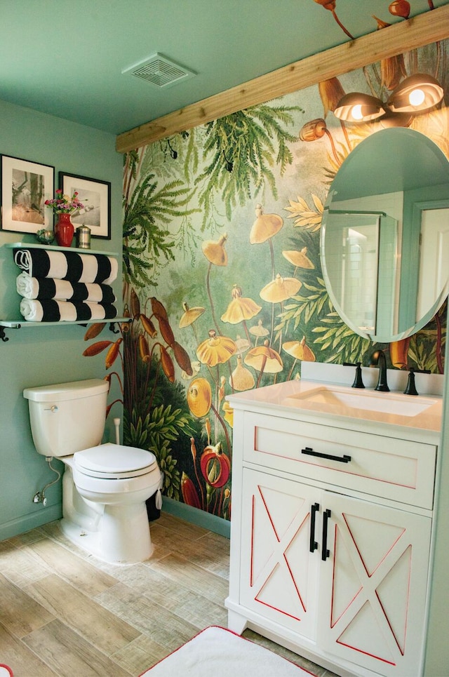 bathroom featuring visible vents, toilet, vanity, wood finished floors, and baseboards